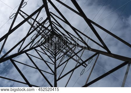 Looking Upward In The Center Of A Large Tall Massive High Voltage Pylon Mast Against Partly Cloudy B