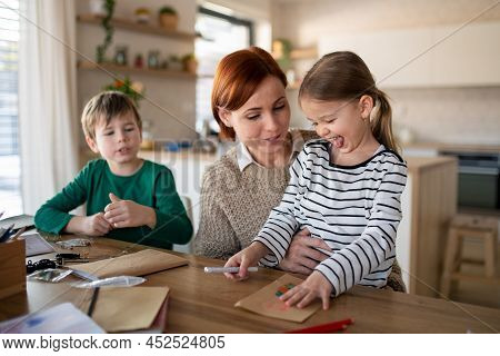Mother Of Little Children Supervising Them When Diong Homework At Home.