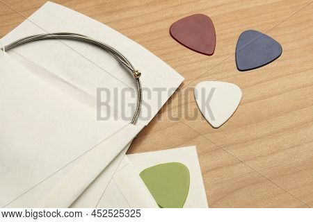 Brand New Guitar String And Some Guitar Picks On A Wooden Table