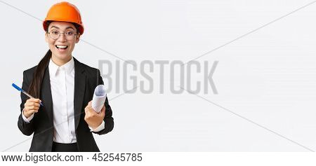Smiling Professional Female Architect, Asian Engineer In Helmet And Business Suit, Holding Blueprint