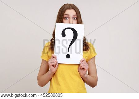 Young Surprised Female Holding White Billboard With Question Mark On It, Covering Half Of Face With,