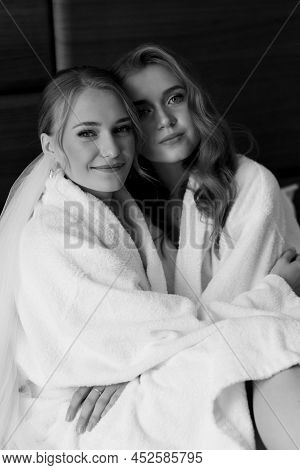 Young Beautiful Models Sit On The Bed In White Coats. Black And White Photo
