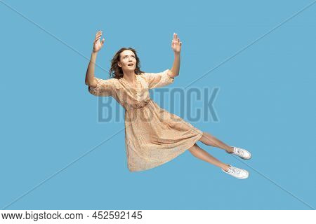 Hovering In Air. Full Length Beautiful Pensive Girl In Yellow Dress Levitating Flying In Mid-air, Lo