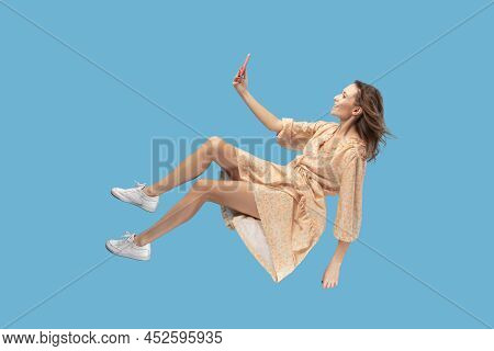 Hovering In Air. Smiling Girl In Yellow Dress Levitating With Mobile Phone, Reading Message Chatting