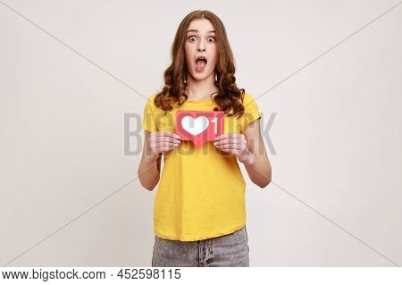 Like And Follow My Blog. Shocked Blogger Young Woman In Yellow T-shirt Holding Social Media Heart Bu