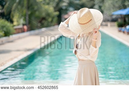 Woman Wearing White Shirt, Long Skirt And Straw Hat Posing Near Swimming Pool.