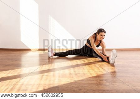 Slim Gymnast Woman Sitting With Spread Legs, Bending To Touch Feet, Doing Stretching Muscle, Wearing