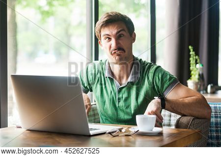 Portrait Of Man Employee Wearing Green T-shirt, Crossing Eyes, Fooling Around And Having Fun, Sittin