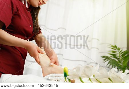 Cropped Photo Of A Masseur Spacialist In Red Uniform Making Feet Massage Procedure To A Client Woman