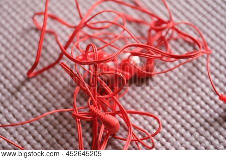 Red Wired Headphones On A Gray Background. Closeup Of Tangled Tangled Tied Ears With White Headphone