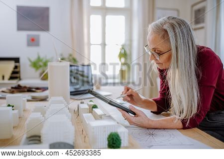 Senior Woman Eco Architect With Model Of Modern Bulidings Working In Office.