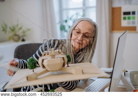 Senior Woman Architect Holding Model Of Modern Eco Buliding In Office