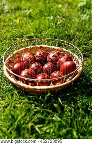 Defocus Closeup Of Basket Of Colored Red Eggs On Nature Green Grass Background. Easter Holiday Conce