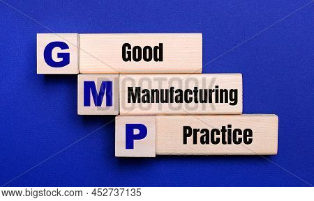 On A Bright Blue Background, Light Wooden Blocks And Cubes With The Text Gmp Good Manufacturing Prac