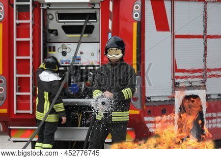 Firefighter During A Drill Extinguishes The Fire And The Fire Truck In The Background