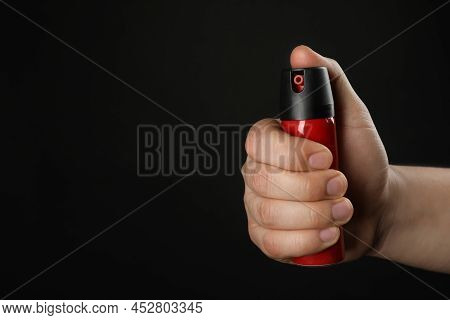 Man Holding Pepper Spray On Black Background, Closeup. Space For Text