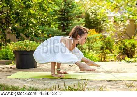 Young Woman Practices Yoga In The Courtyard Of A Country House. Titibhasana.