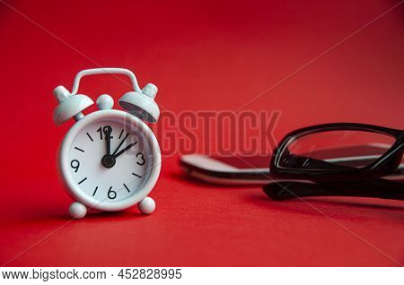 Alarm Clock Pointing At 2 O'clock With Glasses And Phone Background. Copy Space