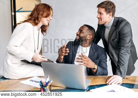 Happy Friendly Coworkers Sitting In Office, Having A Pleasent Conversation. Multiracial Business Peo