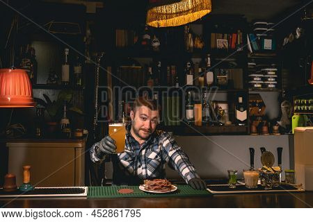 Friendly Smiling Bartenderholding Out Glass Of Unfiltered Beer In Pub