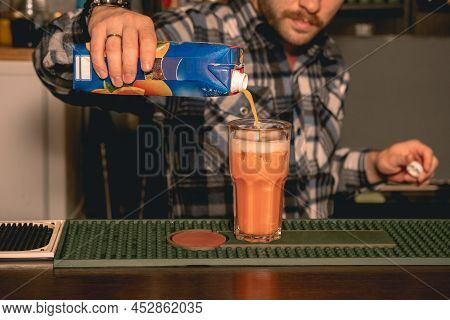 Bartender Pouring Orange Juice To Tall Glass With Ice
