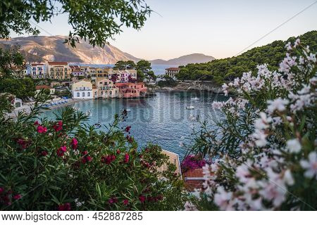 Assos Village On Kefalonia Island, Greece. Red And White Oleandre Flower Blossom In Foreground With 