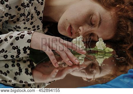 Young Woman Lying With Her Eyes Closed And Touching The Flower Lying On Wet Mirror