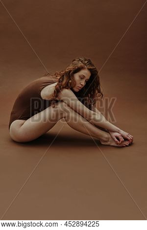 Young Ginger Woman With Curly Hair In Swimsuit Isolated On Brown Background