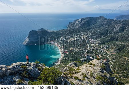 Man Traveller At The Top Of Falcon Sokol Mountain Enjoying Novyi Svit Town Below. Crimea