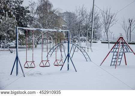 Old Children Playground, Slides And Swings, In A Park Covered In Snow In Serbia, In Eastern Europe, 