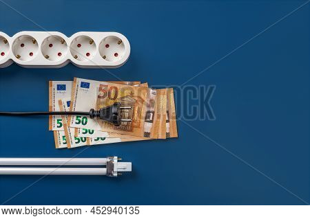 Electric Plug On 50 Euro Banknotes, Power Strip And Compact Fluorescent Light Bulb Over Blue Backgro