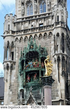 Golden Statue Of Holy Mary With Baby Jesus And The Rathus On  Background In Munich In Germany In The