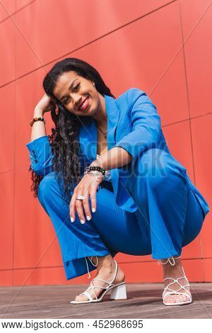 Full Body Of Smiling African American Female In Blue Suit And Shoes Looking At Camera While Hunkerin