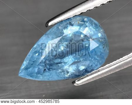 Natural Gemstone Blue Aquamarine In Tongs On A Gray Background
