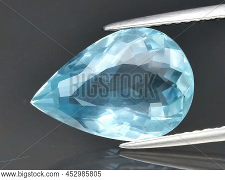 Natural Gemstone Blue Aquamarine In Tongs On A Gray Background