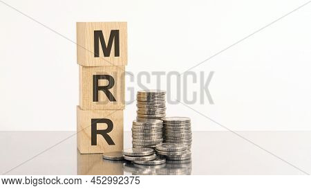 The Word Mrr Is Laid Out Of Wooden Cubes With Letters On White Background With Coins. Mrr - Short Fo