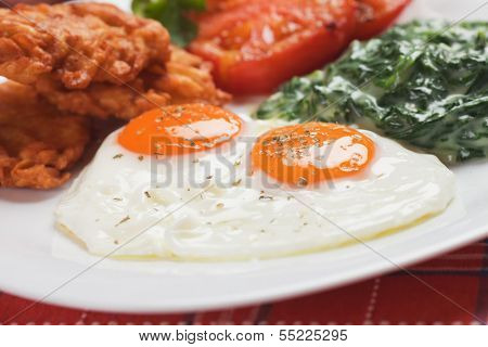 Fried eggs served for breakfast with spinach, fried tomato and potato pancakes