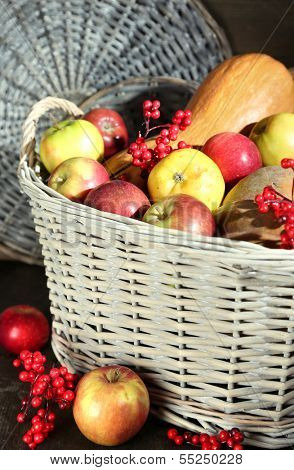 Juicy apples and pumpkin in wooden basket on table close-up