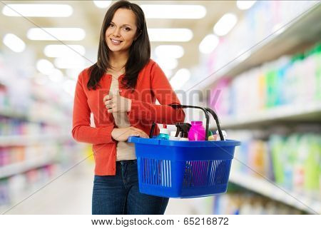 Beautiful cheerful brunette woman with basket full of cleansers in a shop