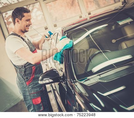 Worker on a car wash cleaning car with a spray