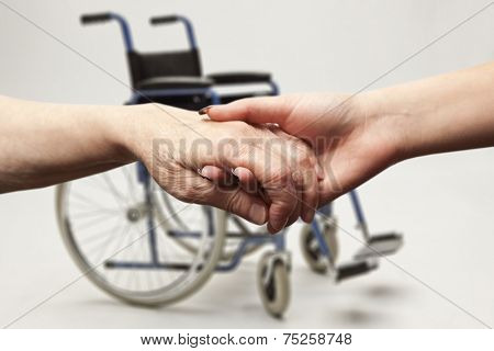 Hands of an elderly woman holding the hand of a younger woman on wheelchair background