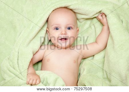 Caucasian baby boy covered with green towel joyfully smiles at camera