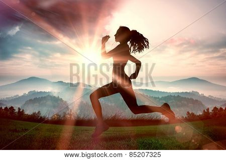 Full length of healthy woman jogging against sun shining over mountains