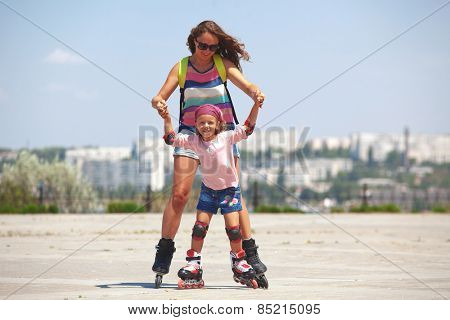 Young mother with her 5 years old daughter rollerskating in park