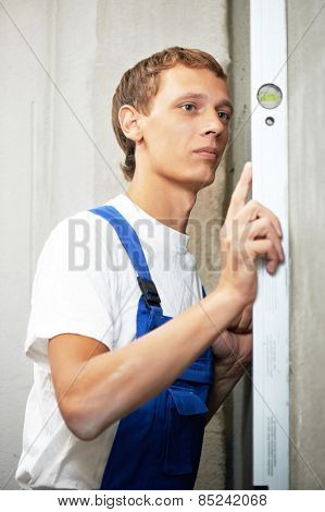 Young plasterer worker checking wall with level before wallboard installation