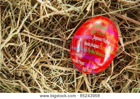 Happy easter in different languages against red egg on straw