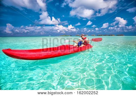 Young caucasian attractive man with his little son kayaking on tropical island.