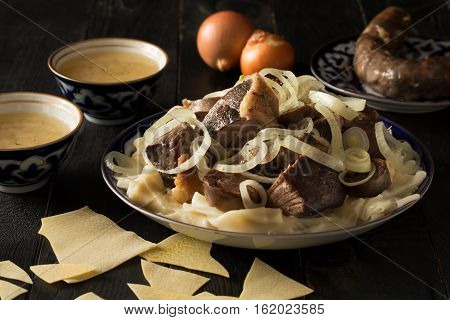 National Kazakh dish - Beshbarmak prepared with meat and pasta on the dark wooden table