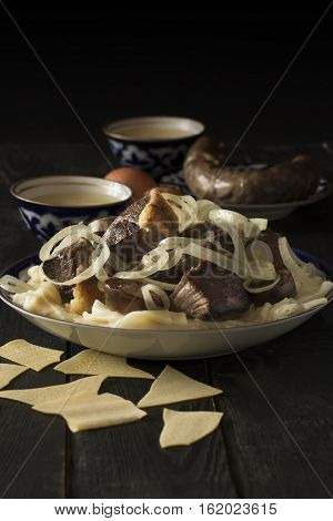 National Kazakh dish - Beshbarmak prepared with meat and pasta on the dark wooden table. Vertical orientation