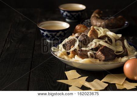 National Kazakh dish - Beshbarmak prepared with meat and pasta on the dark wooden table